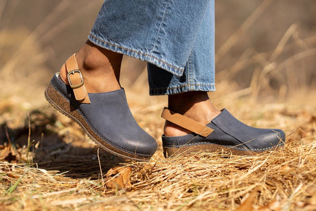 Blue clogs with brown straps worn outdoors on a blurred natural background