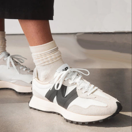 White New Balance sneakers with a black logo worn by a person on a blurred background