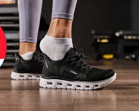 Person wearing black athletic shoes with white soles on a wooden floor.