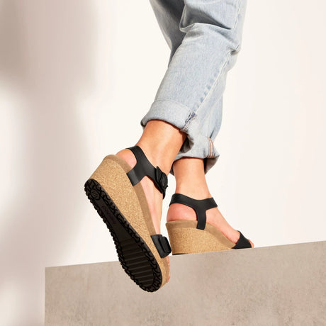 Black wedge sandals with cork soles worn by a person in light blue jeans.