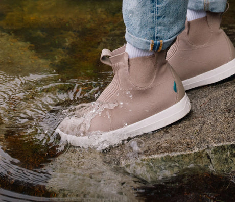 Brown waterproof Vessi sneakers with white soles worn by a person standing in water.