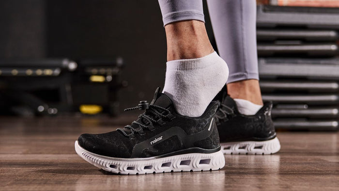 Person wearing black athletic shoes with white soles on a wooden floor.