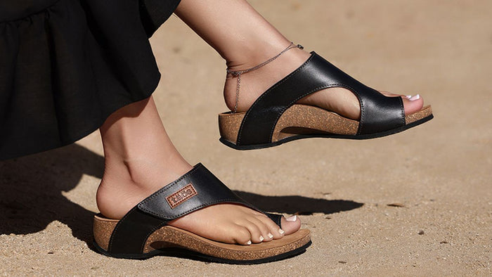 Black sandals with cork soles worn on a sandy surface